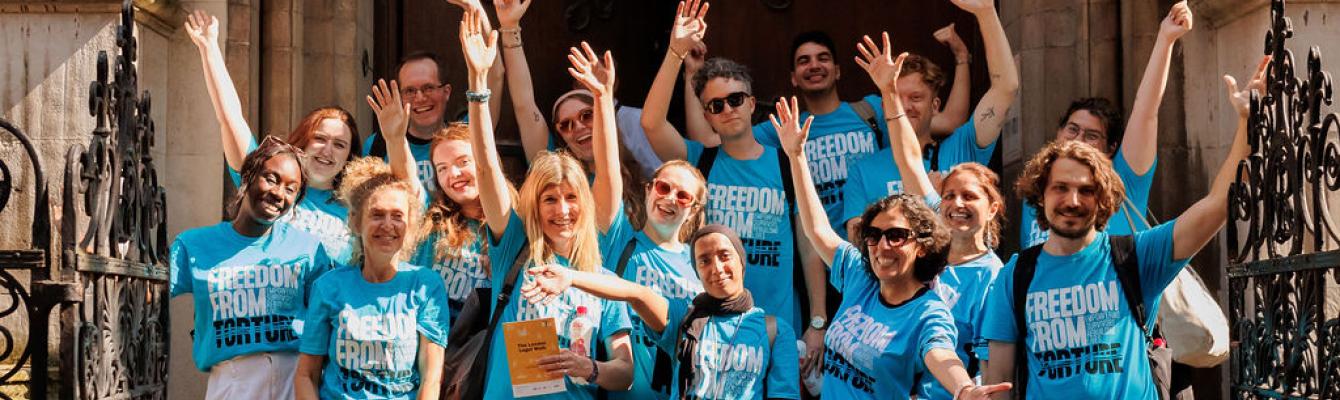 a big group of people in Freedom from Torture t-shirts with their arms up