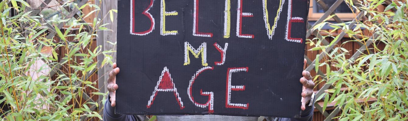 Person holding a placard that reads 'Believe my age'