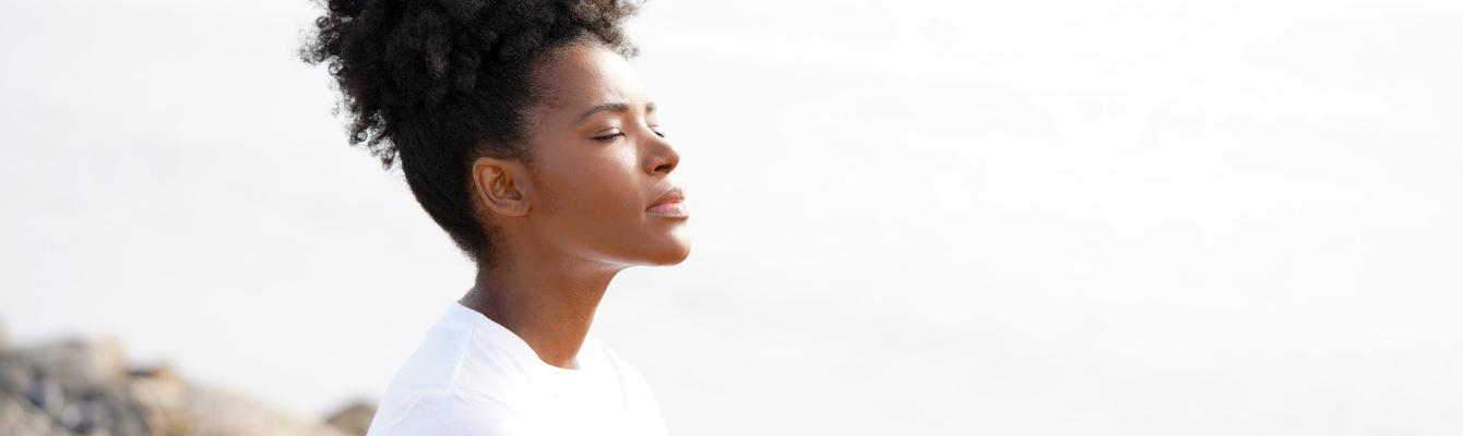 Woman with eyes closed, meditating by a beach