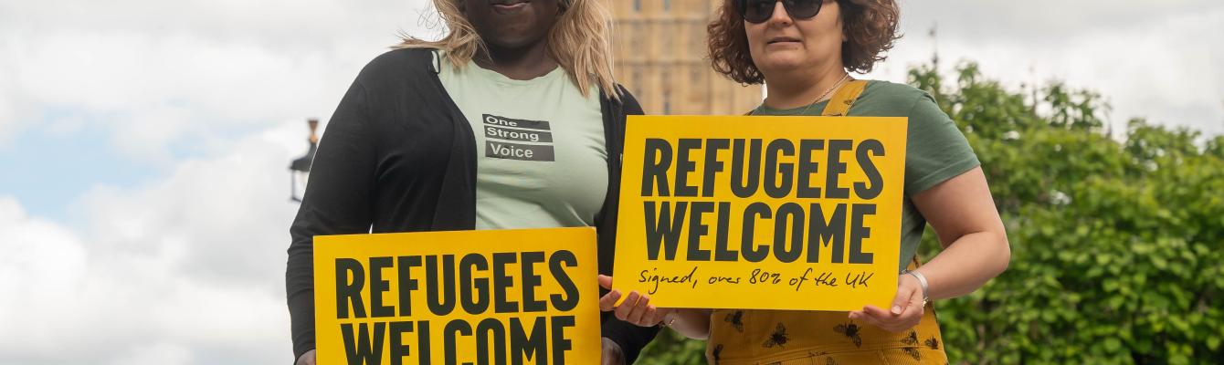 Two women holding a 'Refugees Welcome' sign outside Parliament