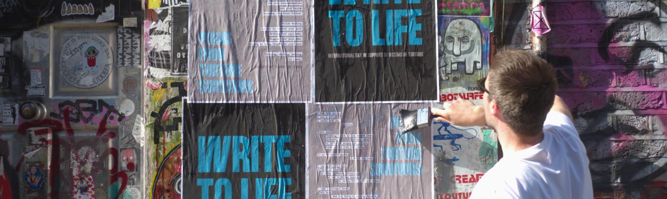 Young man plastering some posters with 'Write to Life' written on them