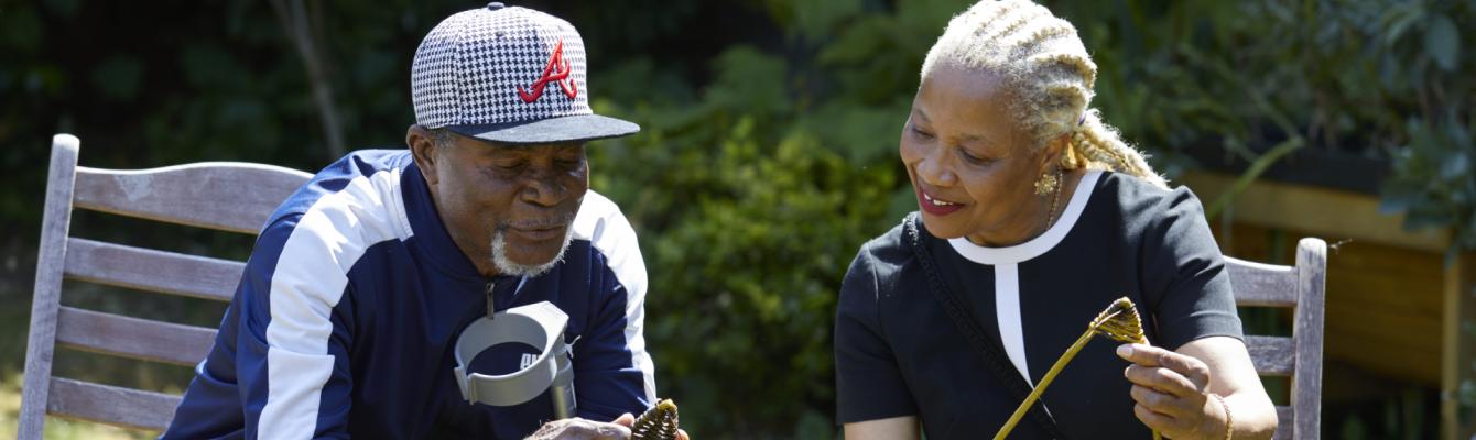 A man and a woman smile as they learn weaving in a sunny garden