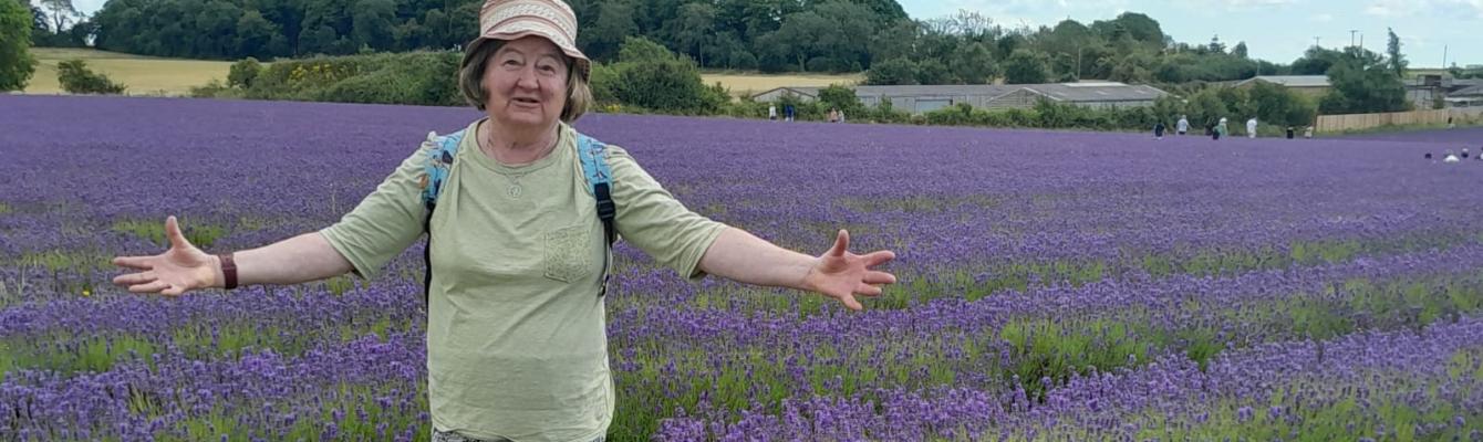Older woman standing in fields, smiling and arms spread