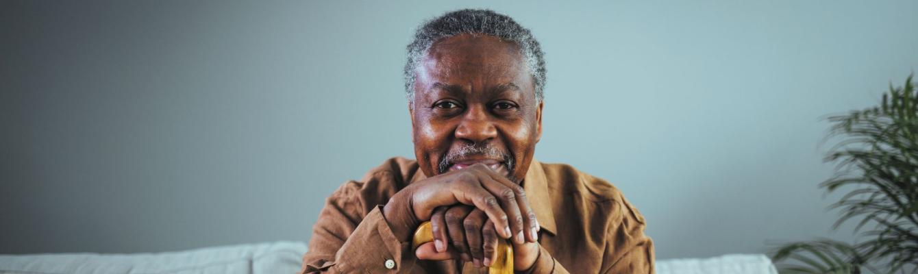 Older black man with walking stick looking into camera