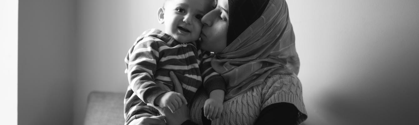 Black and white image of mother cuddling baby wearing a headscarf and both smiling