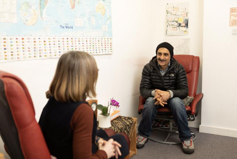A client and a therapist sit facing each other having a one-to-one therapy session.