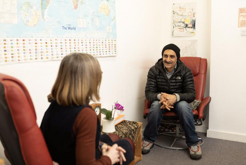 A client and a therapist sit facing each other having a one-to-one therapy session.