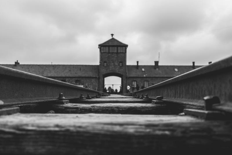 A black and white image of the railway tracks leading up to the entrace of Auschwitz-Birkenau, former Nazi German concentration and extermination camp in Poland.