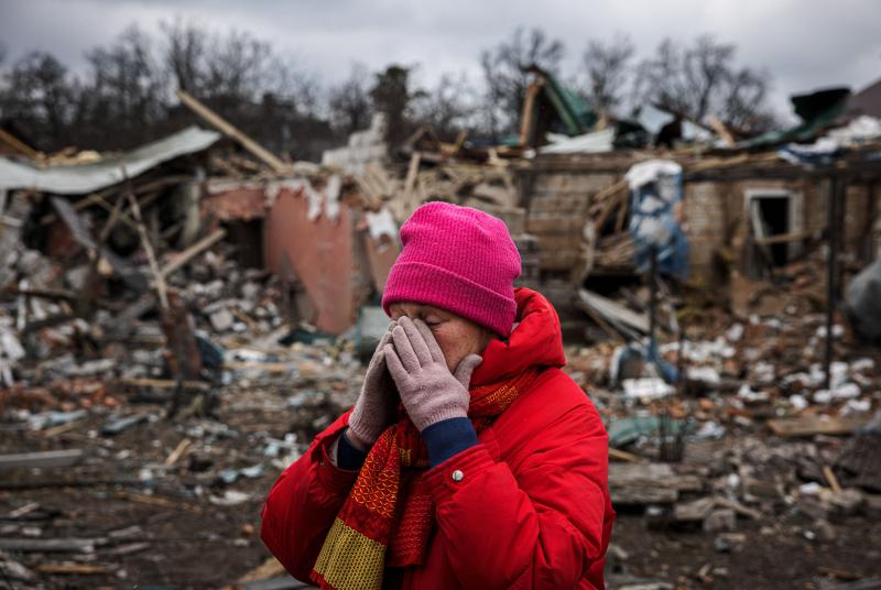Woman in red clothing looking distraught as she's surrounded by destruction