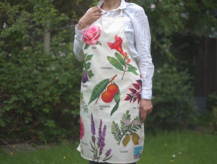 A woman wears a branded apron in a garden