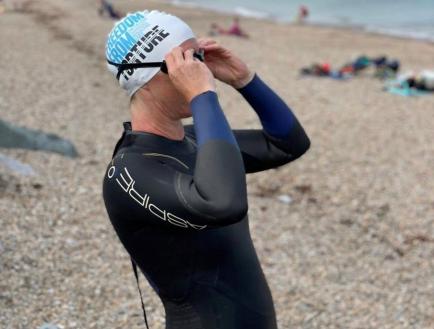 woman in FFT swimming cap and goggles looking out to sea on the beach