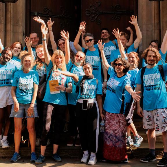 a big group of people in Freedom from Torture t-shirts with their arms up