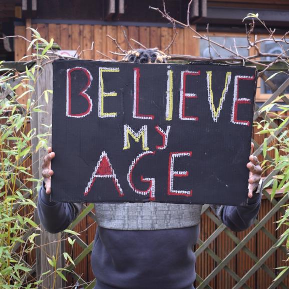 Person holding a placard that reads 'Believe my age'