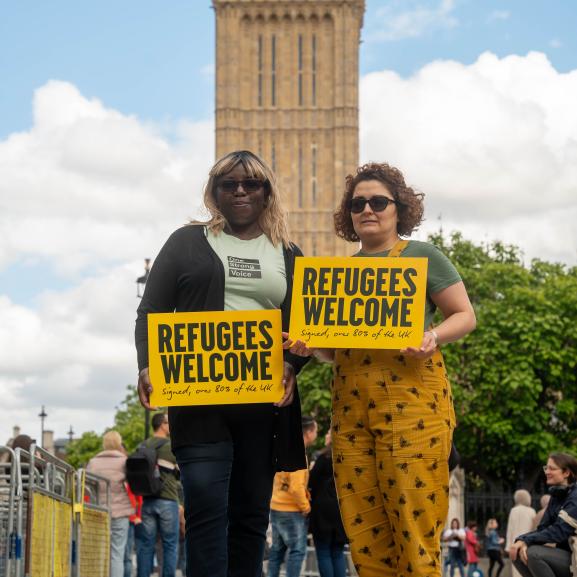 Two women holding a 'Refugees Welcome' sign outside Parliament