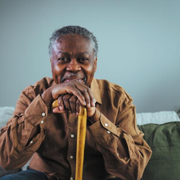 Older black man with walking stick looking into camera