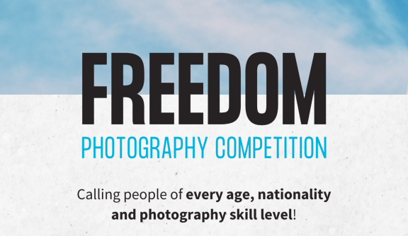 Text reading 'Freedom photography competition'. Freedom is in black and photography competition is in blue with a sky background.