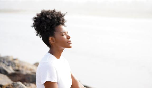 Woman with eyes closed, meditating by a beach