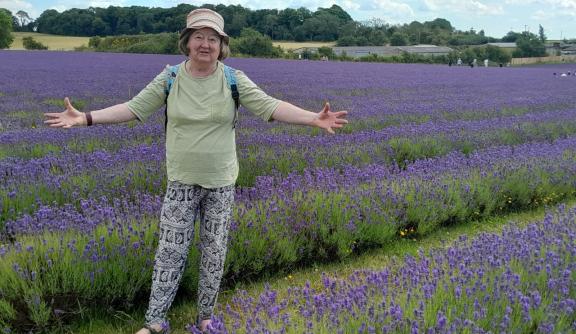 Older woman standing in fields, smiling and arms spread
